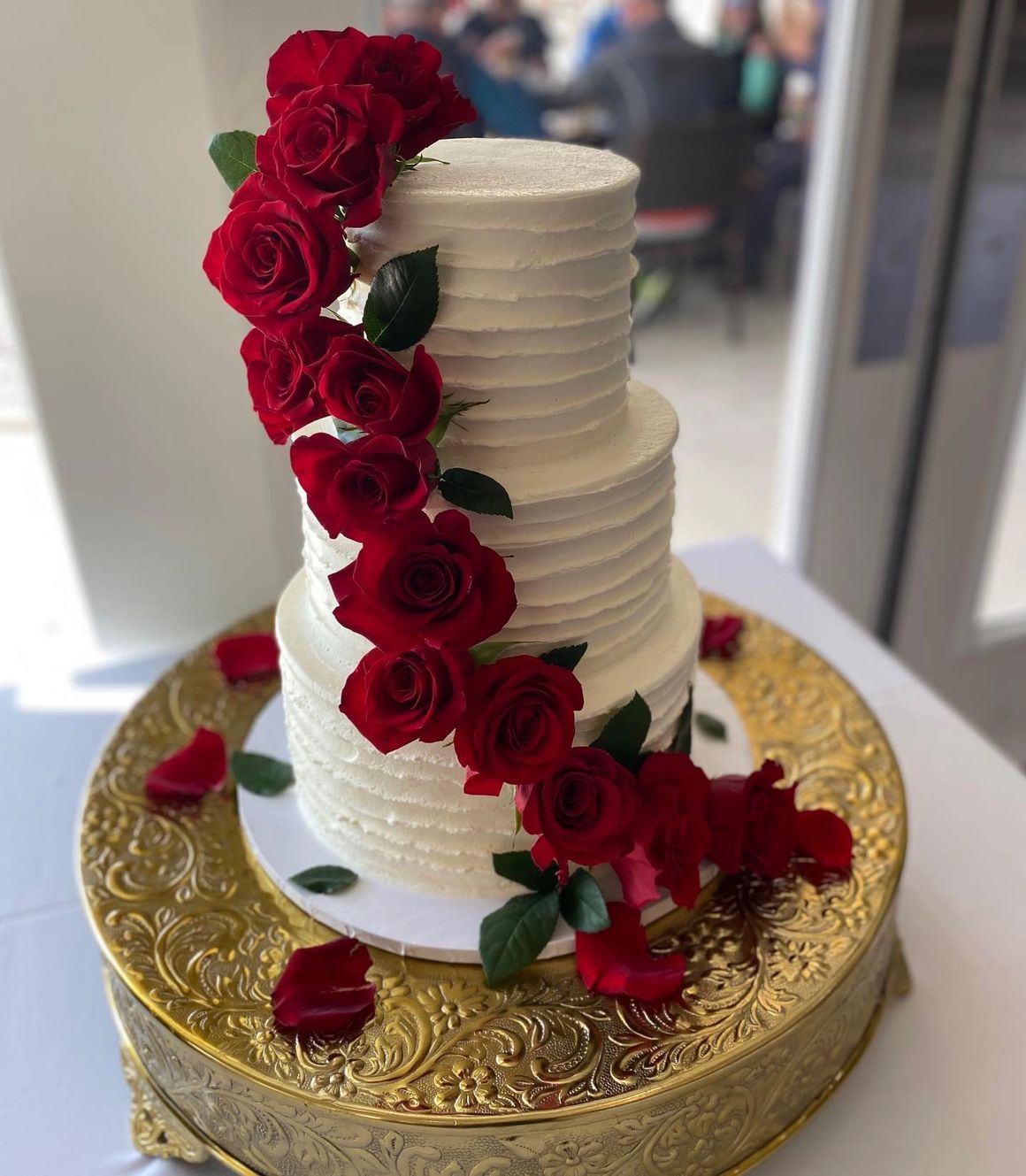 White tiered wedding cake with cascading red roses